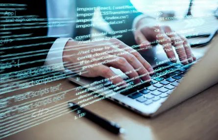 A person typing on a laptop with programming code on the screen.